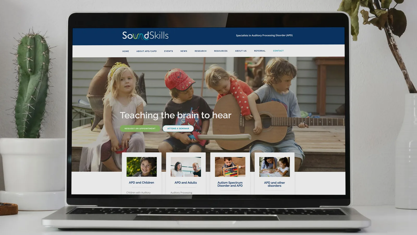 The SoundSkills website Applicable built, open on a laptop on a white desk, with its home page hero and the four Auditory Processing Disorder topic cards. SoundSkills website home page with the line Teaching the brain to hear, shown on a laptop